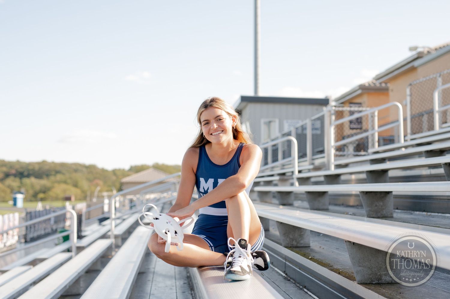 Field hockey player smiles while sitting on stadium bleachers in sunlight.