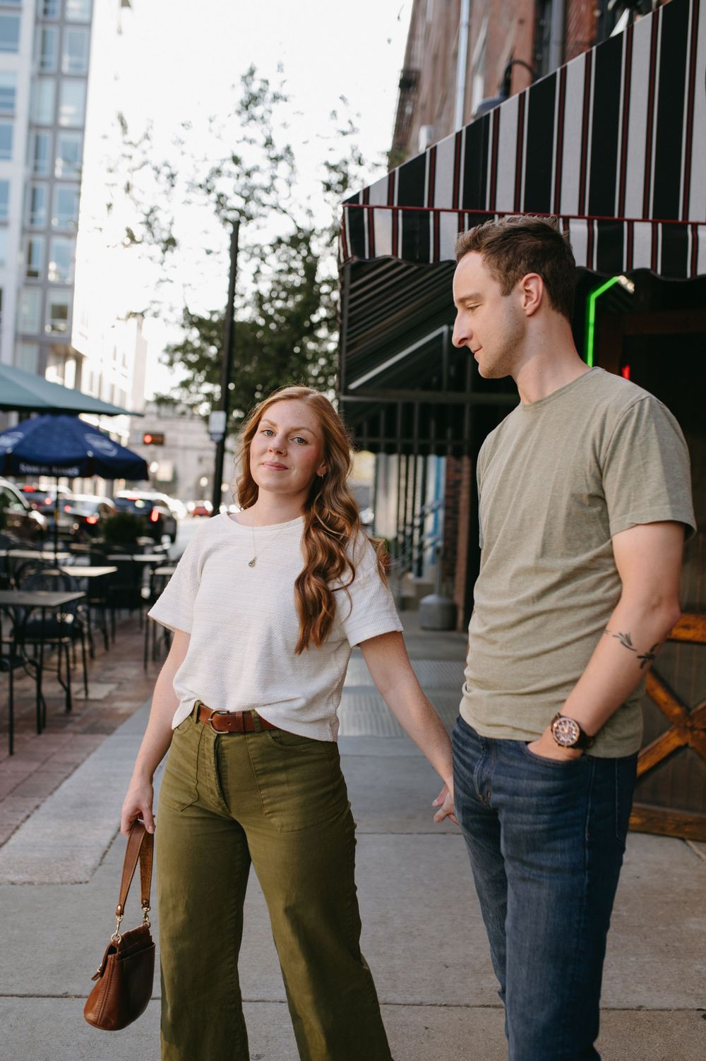 Couple walking on sidewalk outside storefront with striped awning and outdoor seating area.