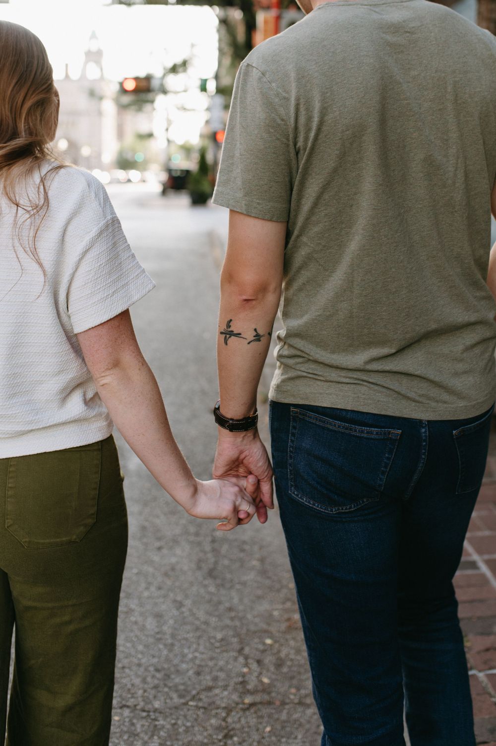 Close-up view of couple holding hands while walking on city sidewalk.
