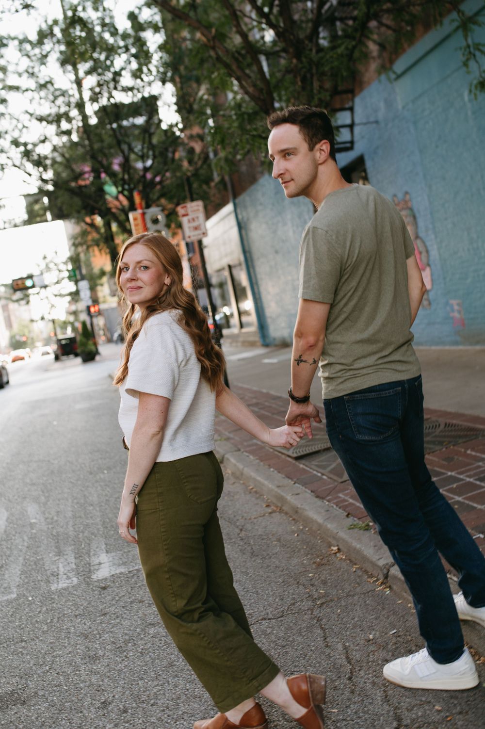 Couple holding hands while walking down urban street with blue wall background.