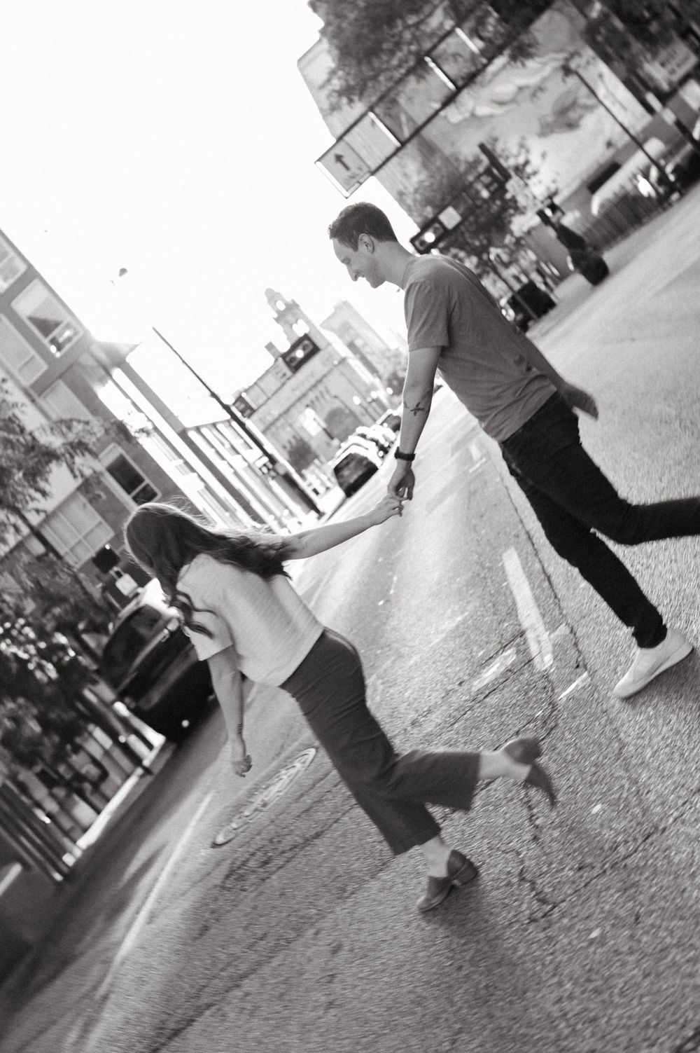 Two people holding hands and dancing on a city street captured in black and white.