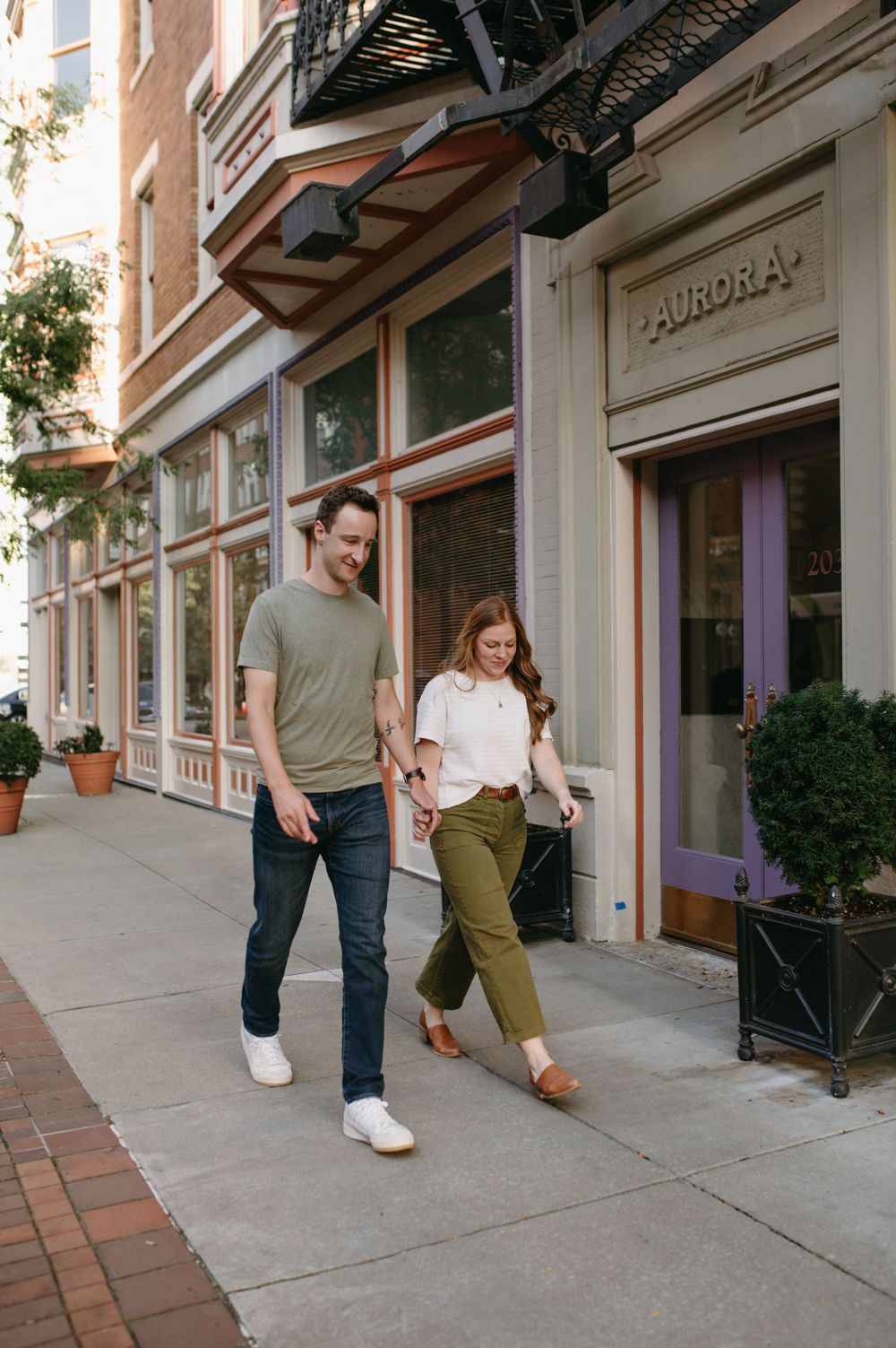 A couple walking together on a sidewalk past storefronts with brick architecture.