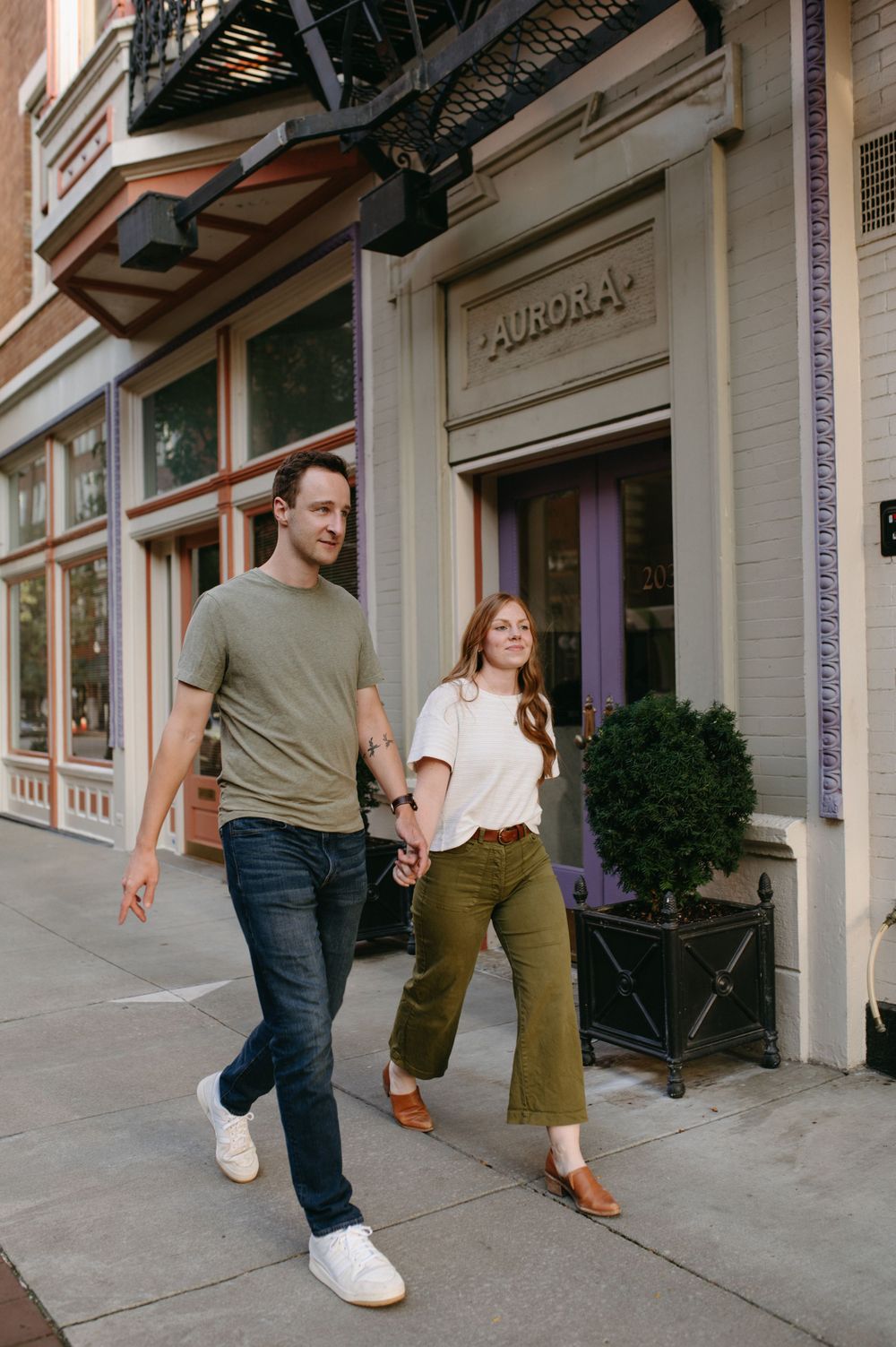 A couple strolls hand in hand past a storefront with 'Aurora' signage.
