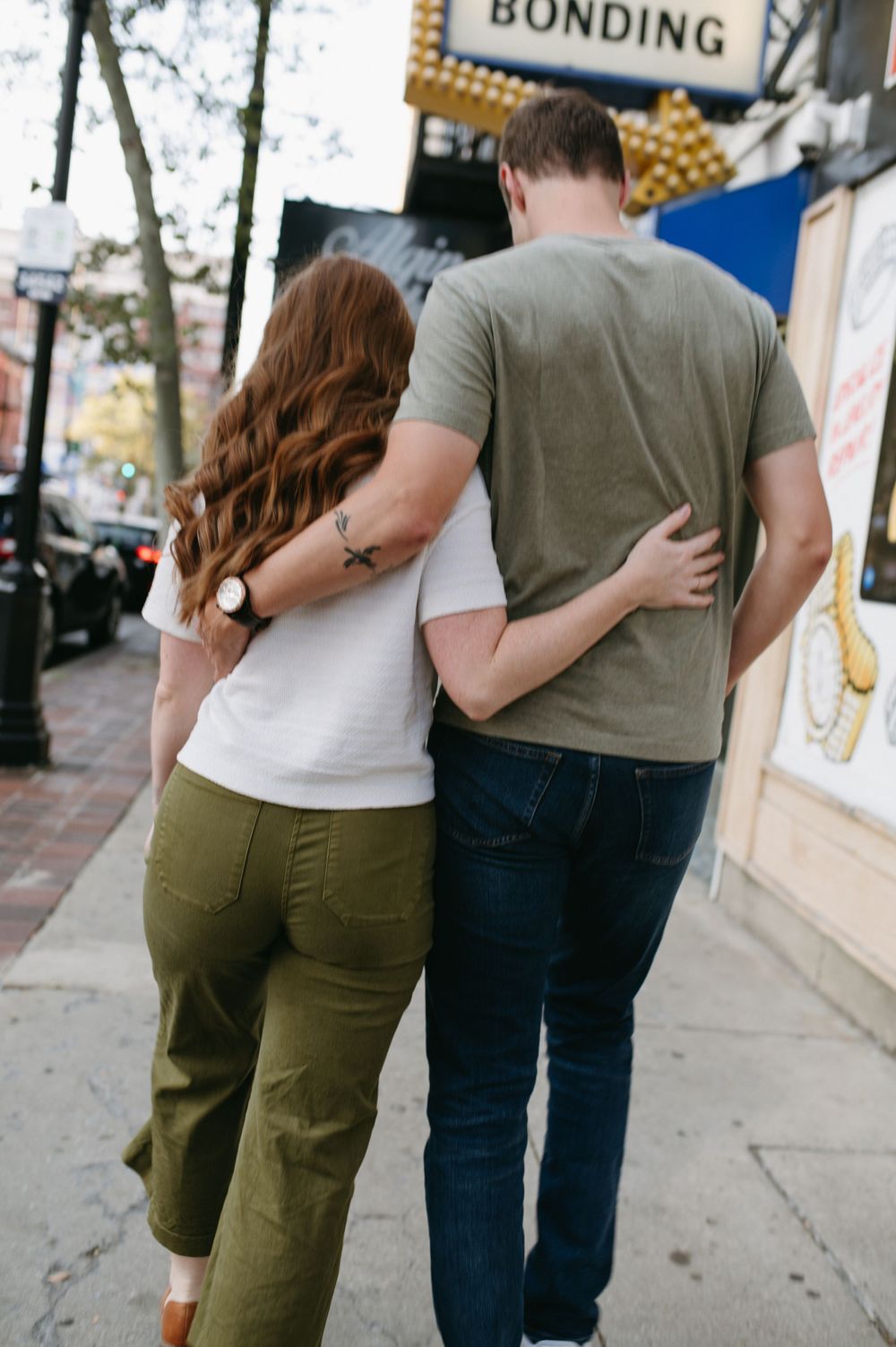 A couple walks arm in arm past a 'Bonding' sign on an urban street.
