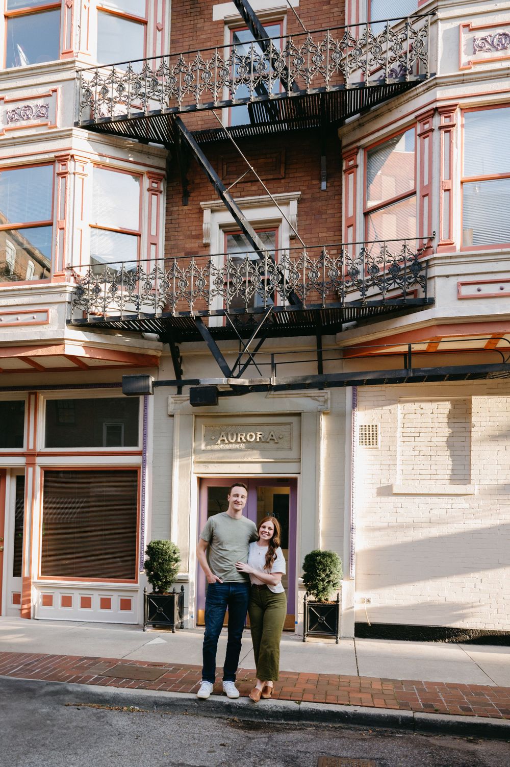 Couple standing together outside historic building with ornate fire escapes and balconies.