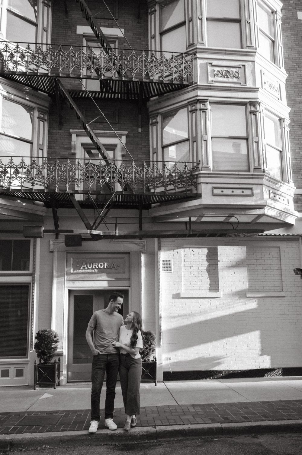 Black and white portrait of a couple outside urban building with decorative iron balconies.