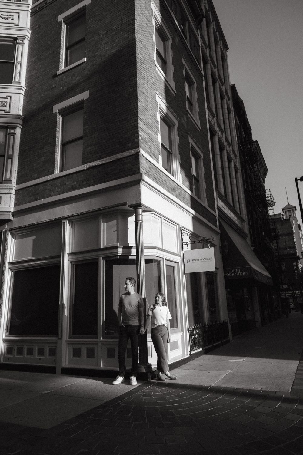 Black and white urban portrait of couple outside historic corner storefront building.