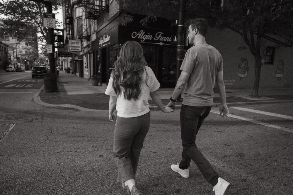 A couple walks hand in hand down a city street in black and white.