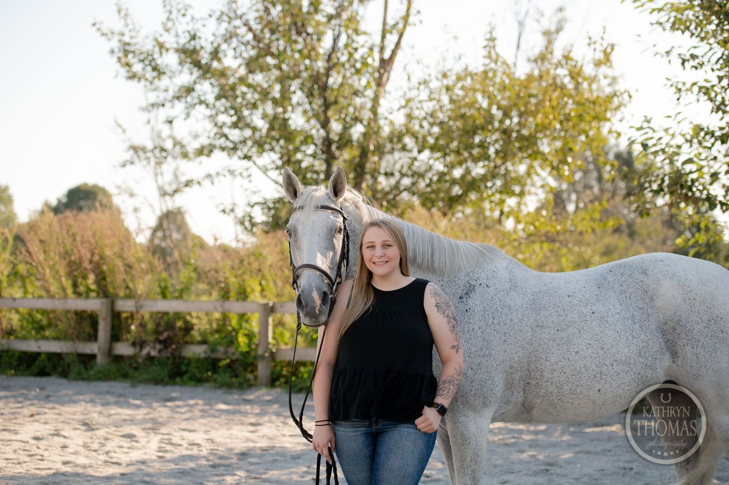 A beautiful grey horse and owner pose together in an outdoor equestrian setting.