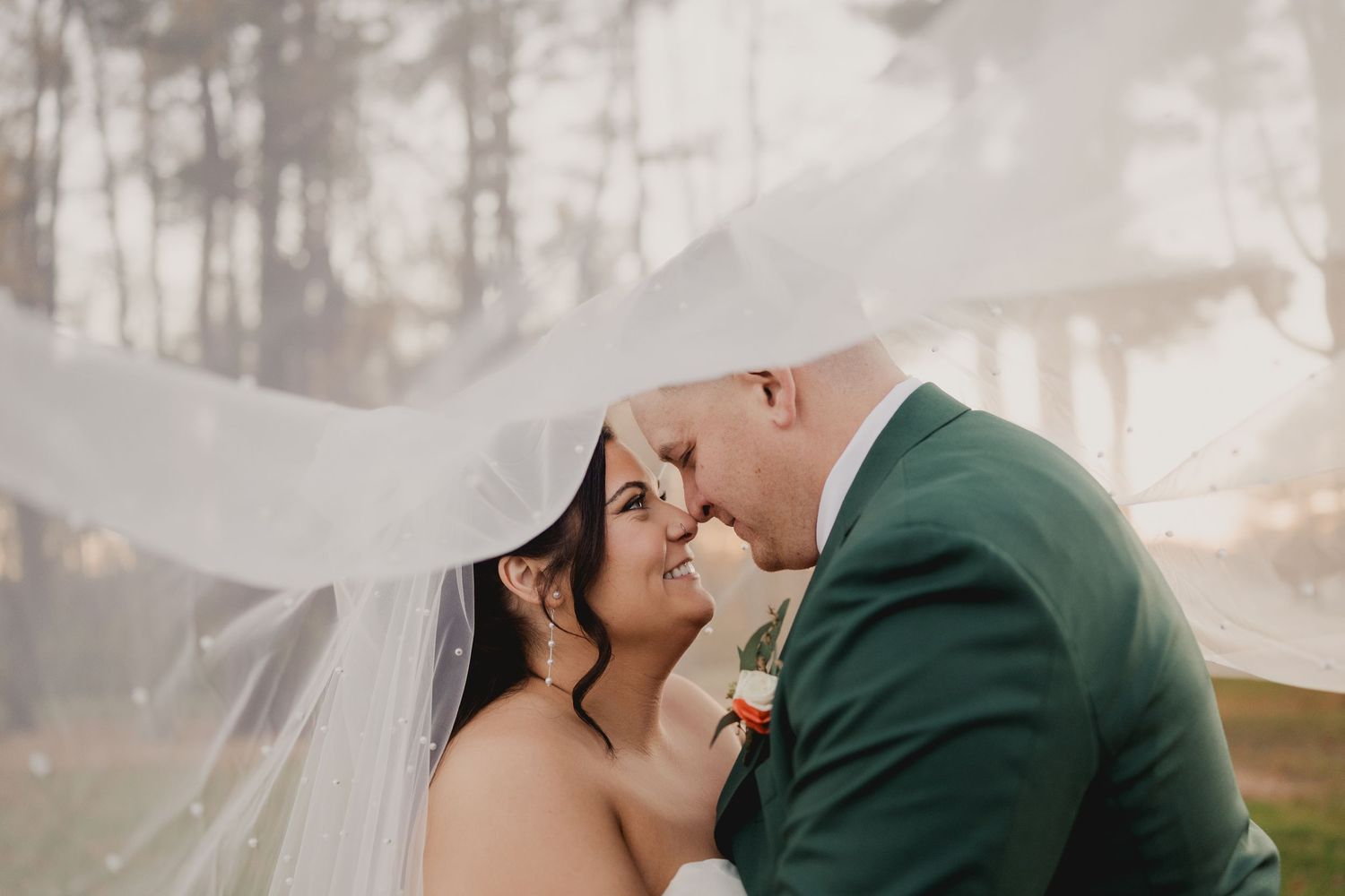 A misty winter wedding portrait with dramatic lighting and bare trees in the background.