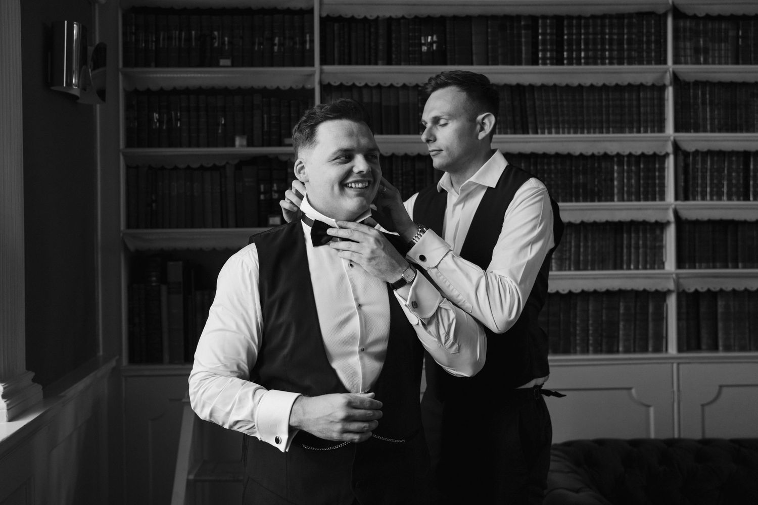groomsman helping groom with bow tie in the library at Iscoyd park