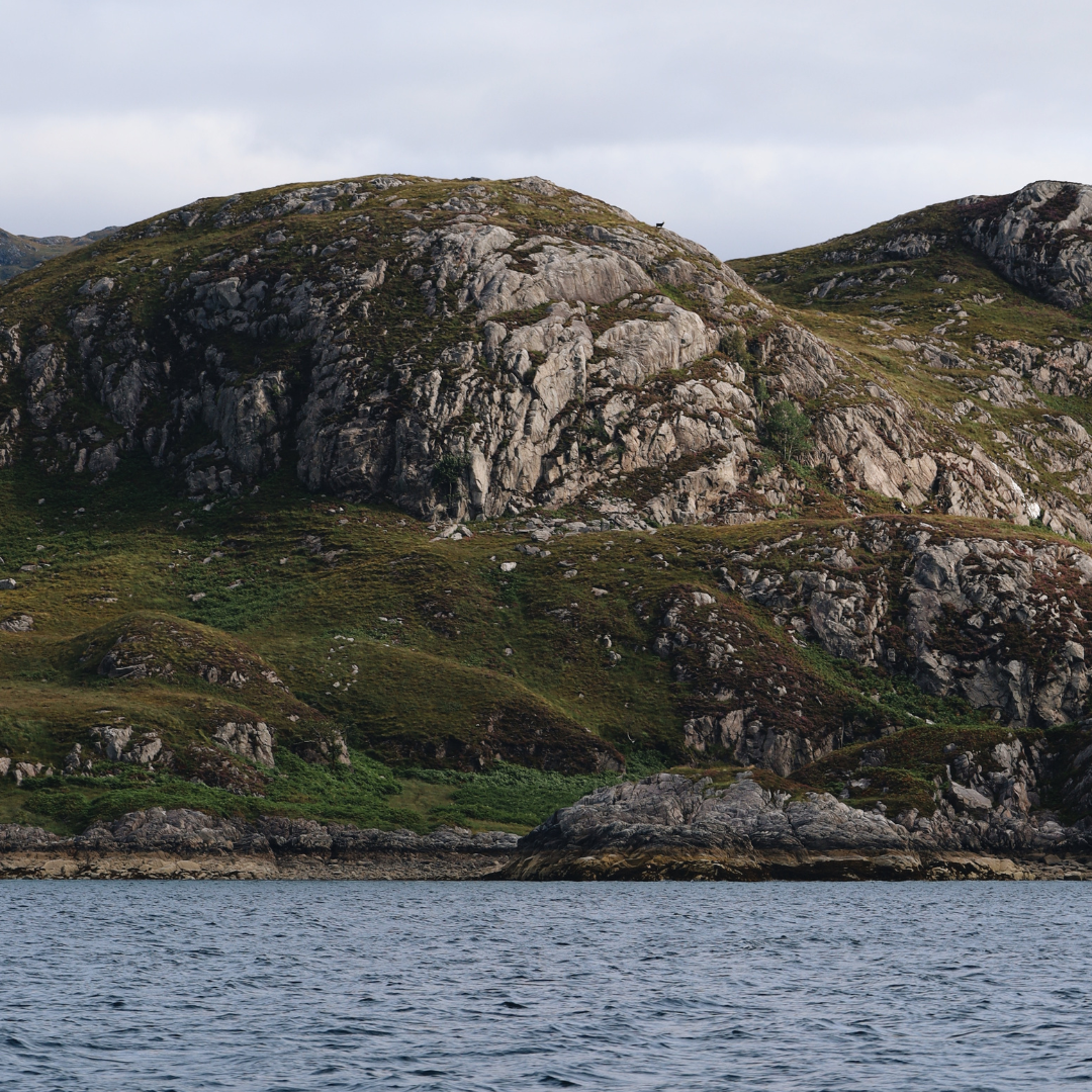 Rocky coastal landscape with rugged cliffs and mountains rising from the sea.