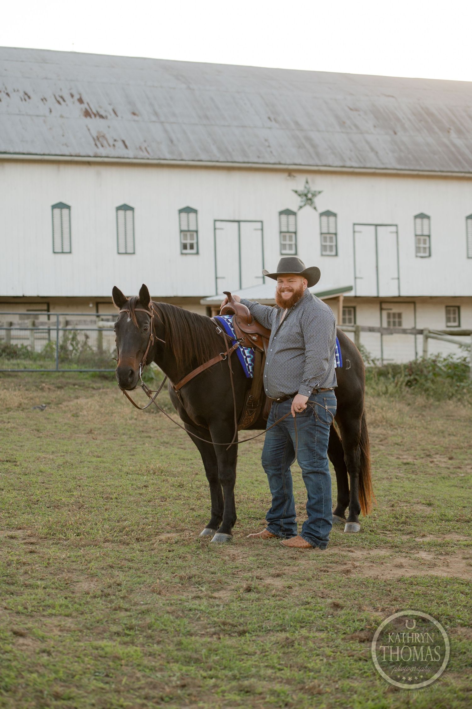 Dark horse with blue saddle pad stands near white barn with star decoration.