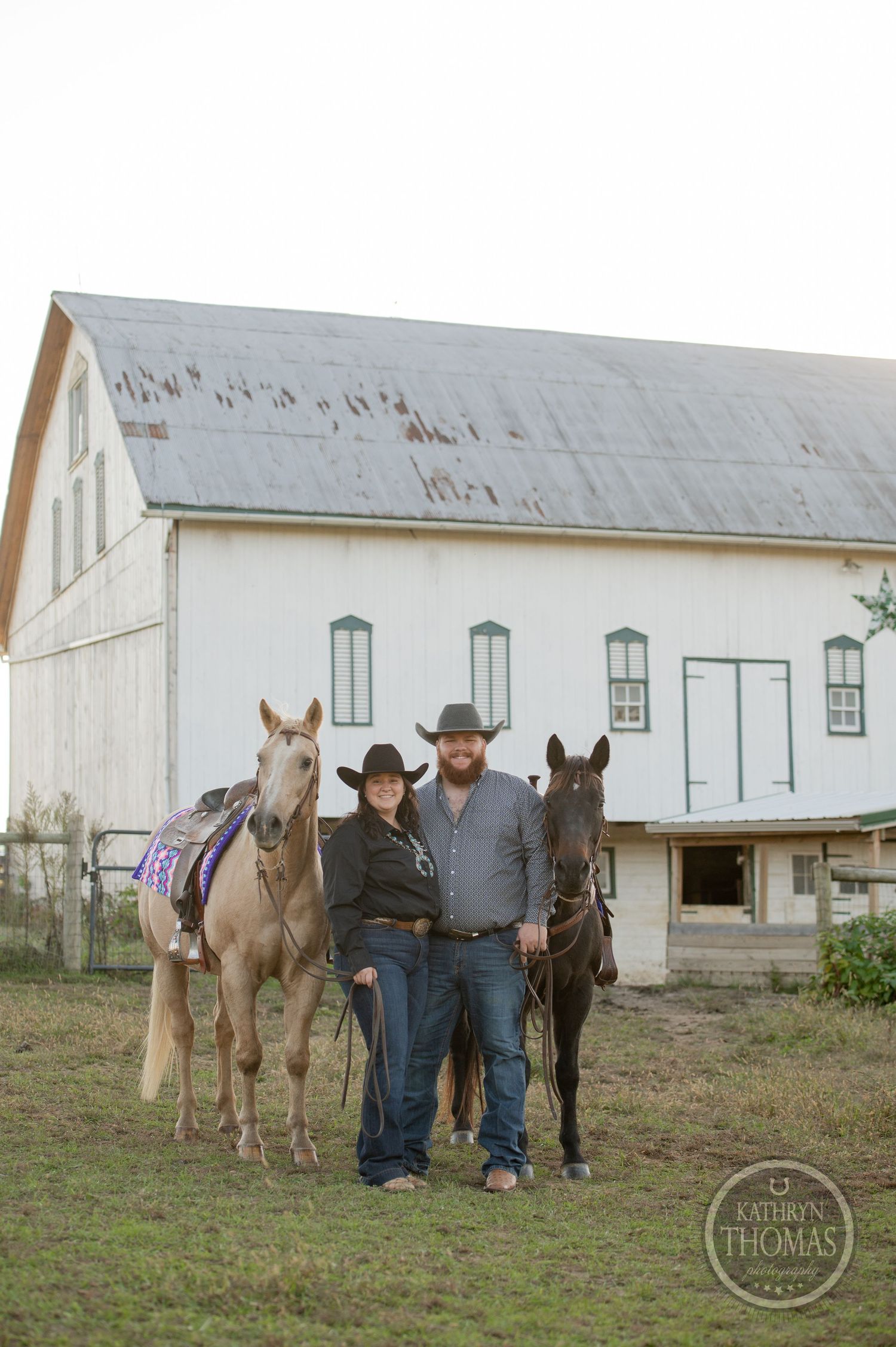 Ranchers pose with palomino and dark horses against white barn backdrop.