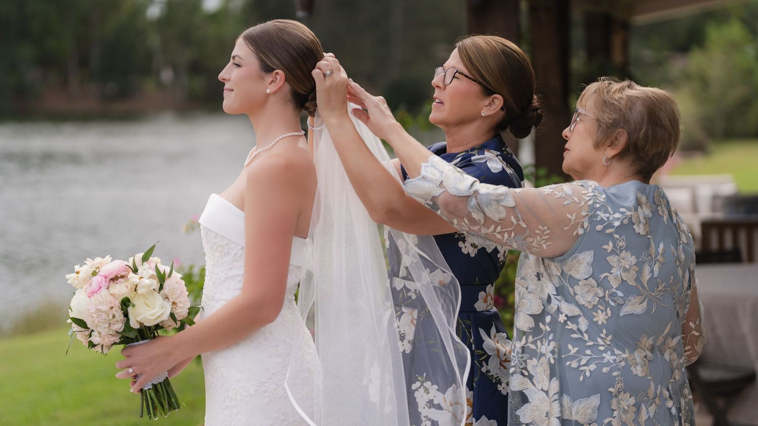 A couple in wedding attire reaches out to pet a curious donkey through a wooden fence.