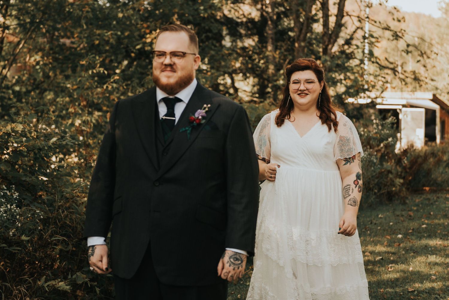 A bride and groom stand together outdoors during a rustic wedding photoshoot on a sunny day.