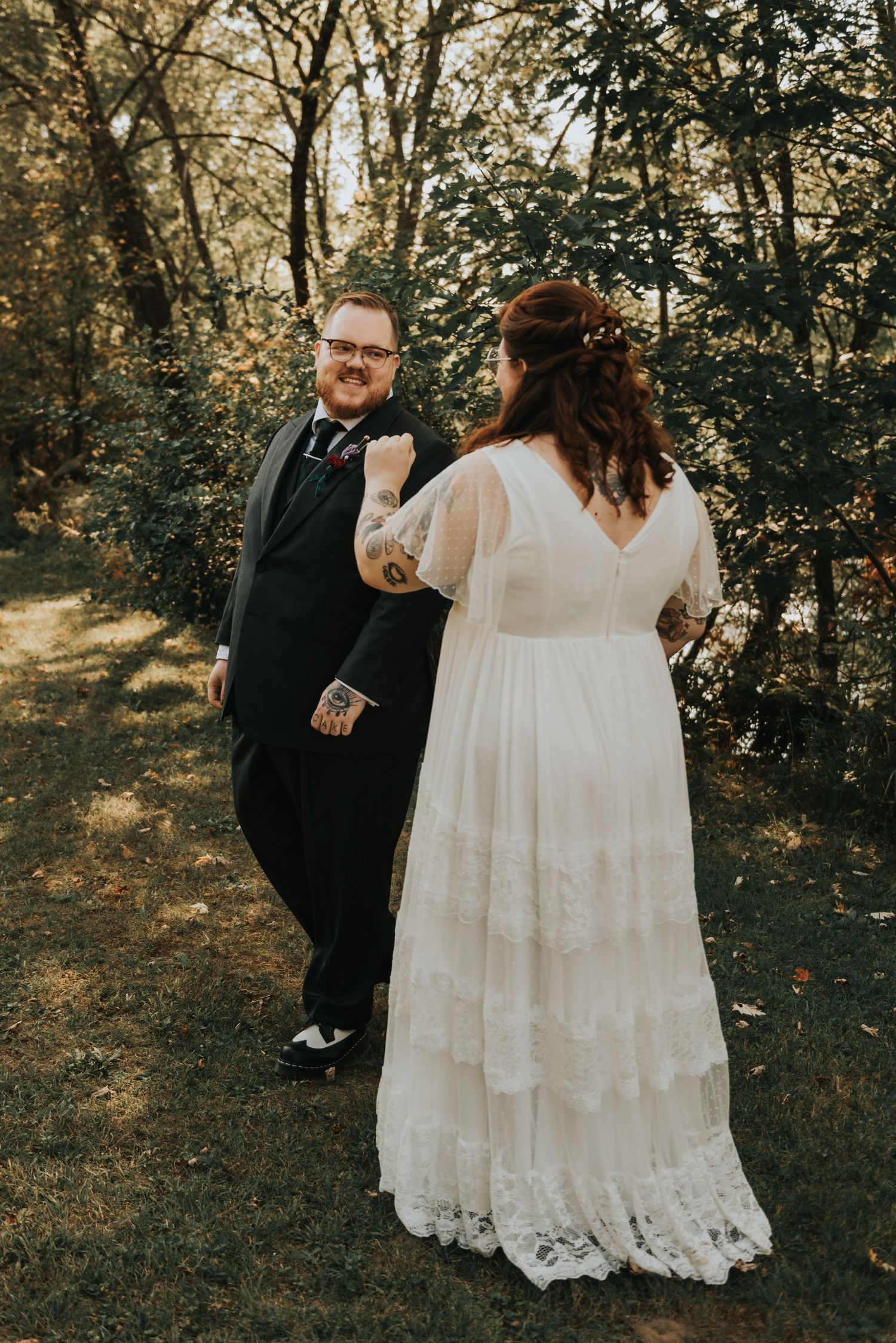 A couple shares a joyful first look moment outdoors in a wooded setting during their autumn wedding celebration.
