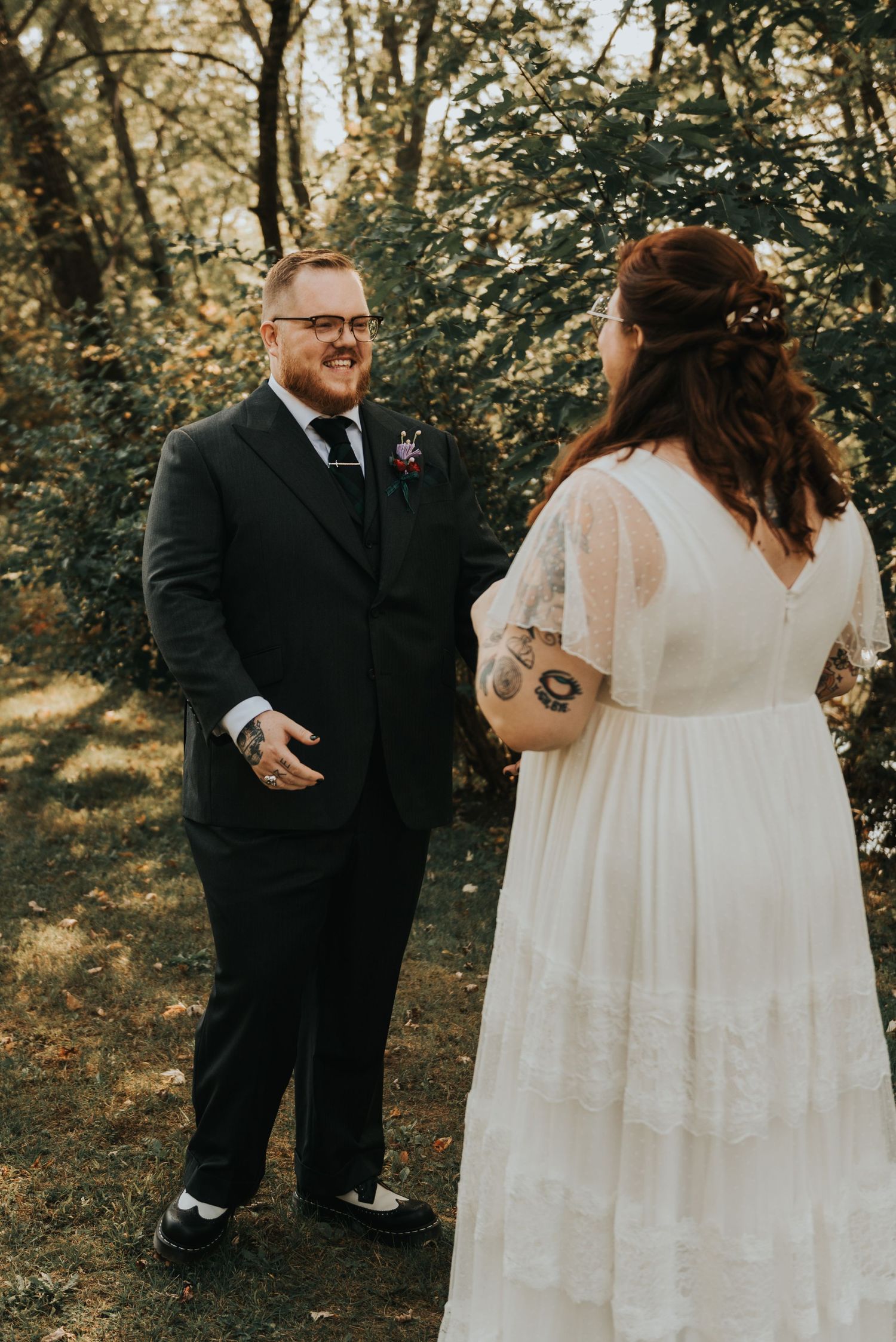 Two people share a candid moment during an outdoor woodland wedding ceremony in sunny natural lighting.