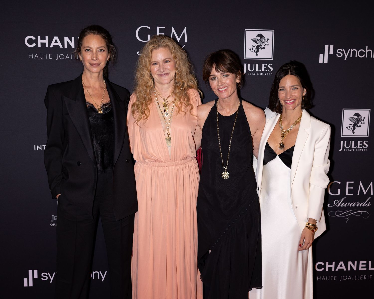 Four people wearing elegant attire pose together at a formal event with Chanel and G.E.M. branding visible in background.