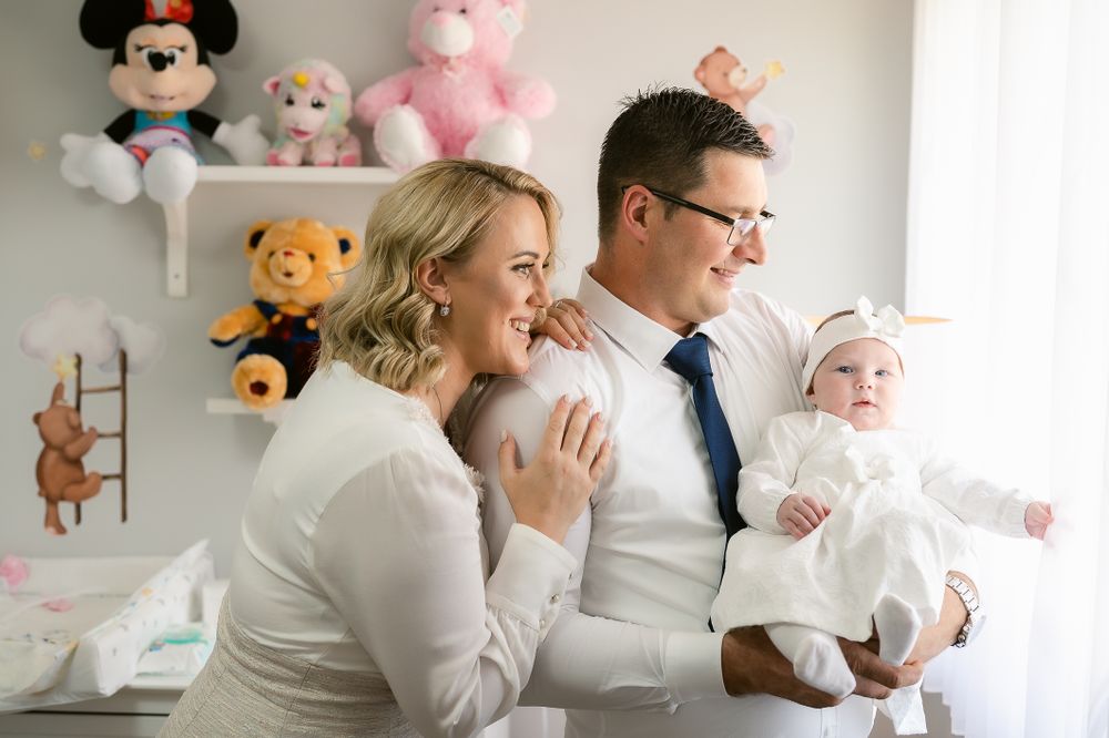 A family enjoys a joyful moment in a nursery decorated with stuffed animals including Mickey Mouse and Winnie the Pooh.