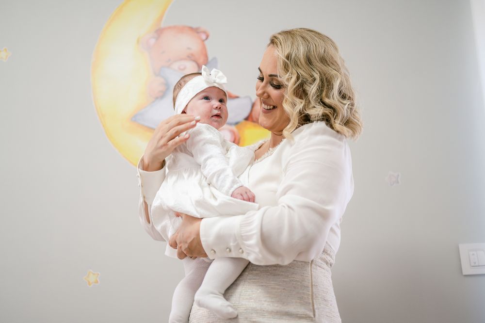 A joyous scene with a baby in white against a moon decoration and a soft pastel background.