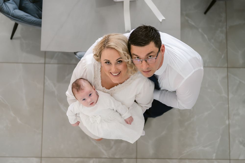 An overhead view of a family dressed in white posing together on a tiled floor.