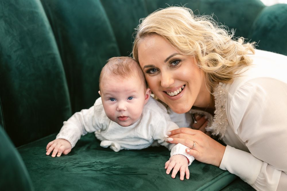 A parent and baby lying together on a plush emerald green velvet couch.