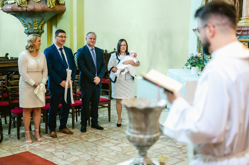 A baptism ceremony taking place in a traditional church interior with attendees gathered around a baptismal font.