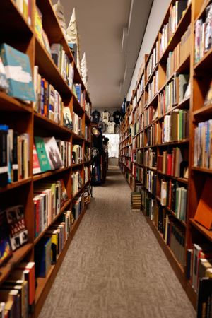 Long narrow aisle between tall wooden library bookshelves filled with books stretching into the distance.