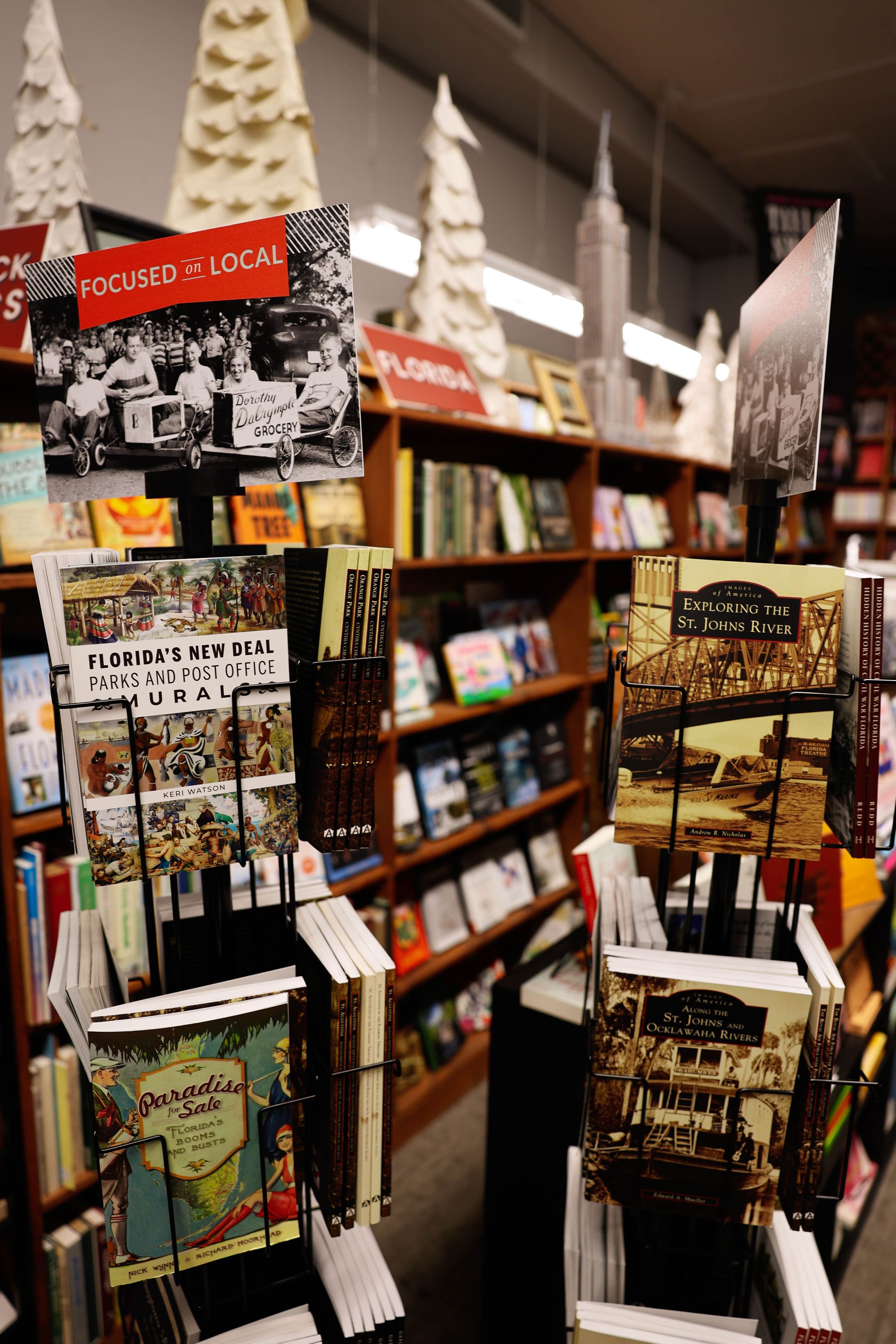 Local postcards and books displayed on wooden shelves at an independent bookstore with festive decorations above.