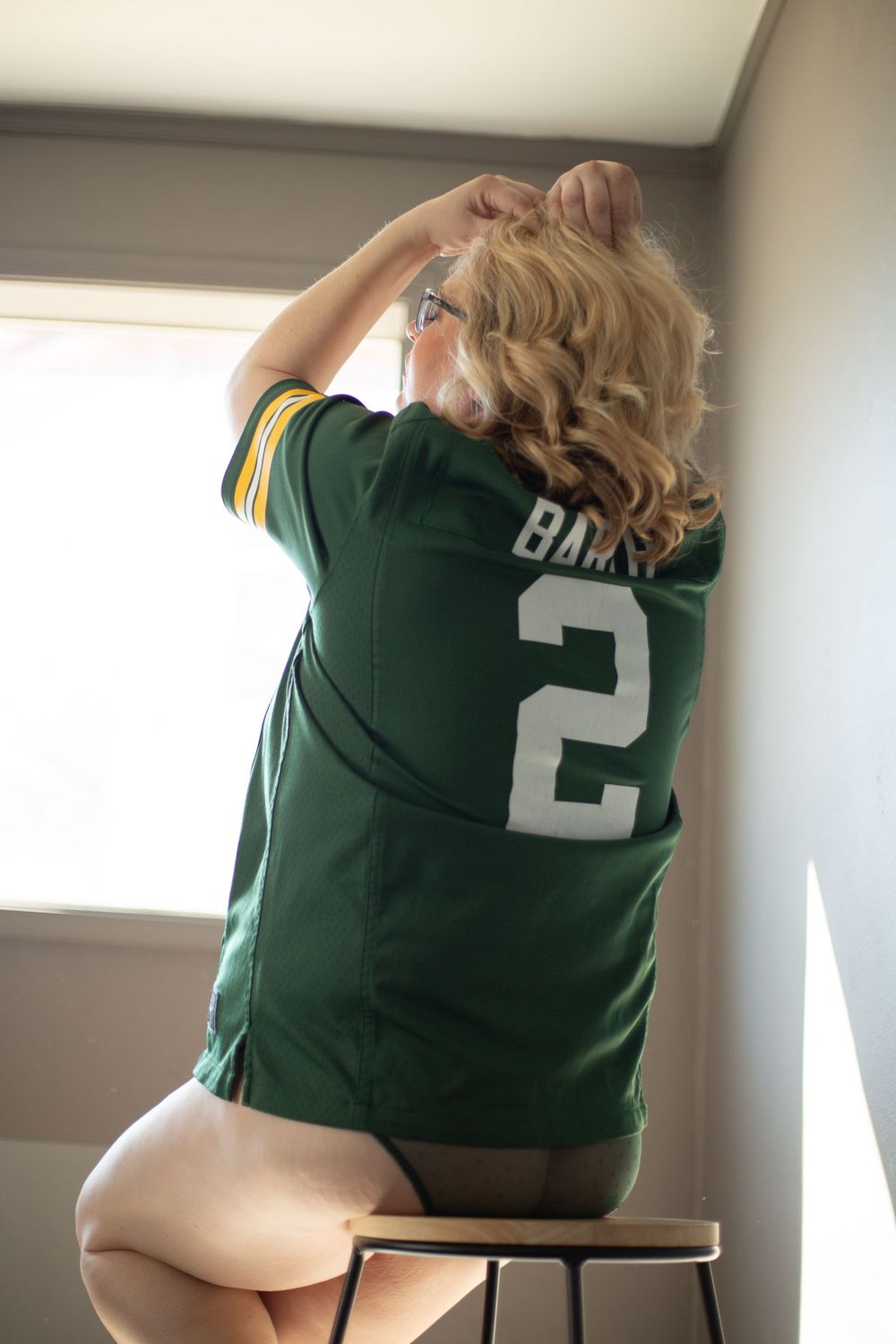 Blonde woman sitting on a stool in a Green Bay Packers jersey and green lace panties.