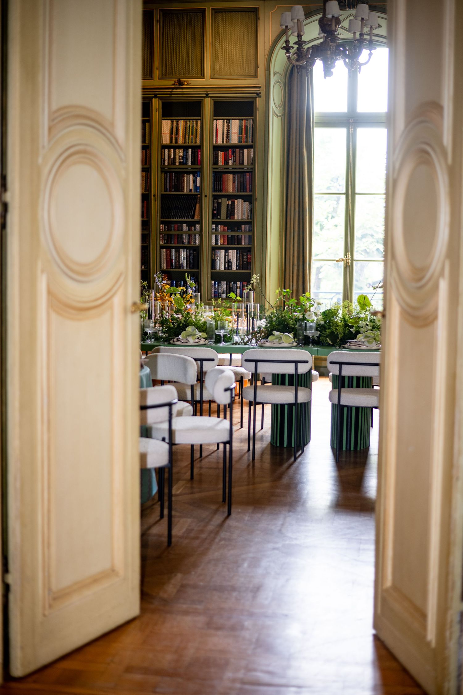 Elegant library room with white doors, floor-to-ceiling bookshelves, green curtains and modern chairs by a bright window. Meridian House DC