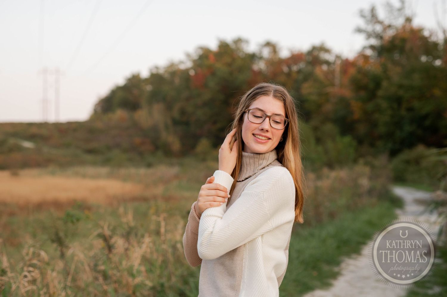 Person in a cozy white turtleneck sweater and glasses poses outdoors during golden hour.