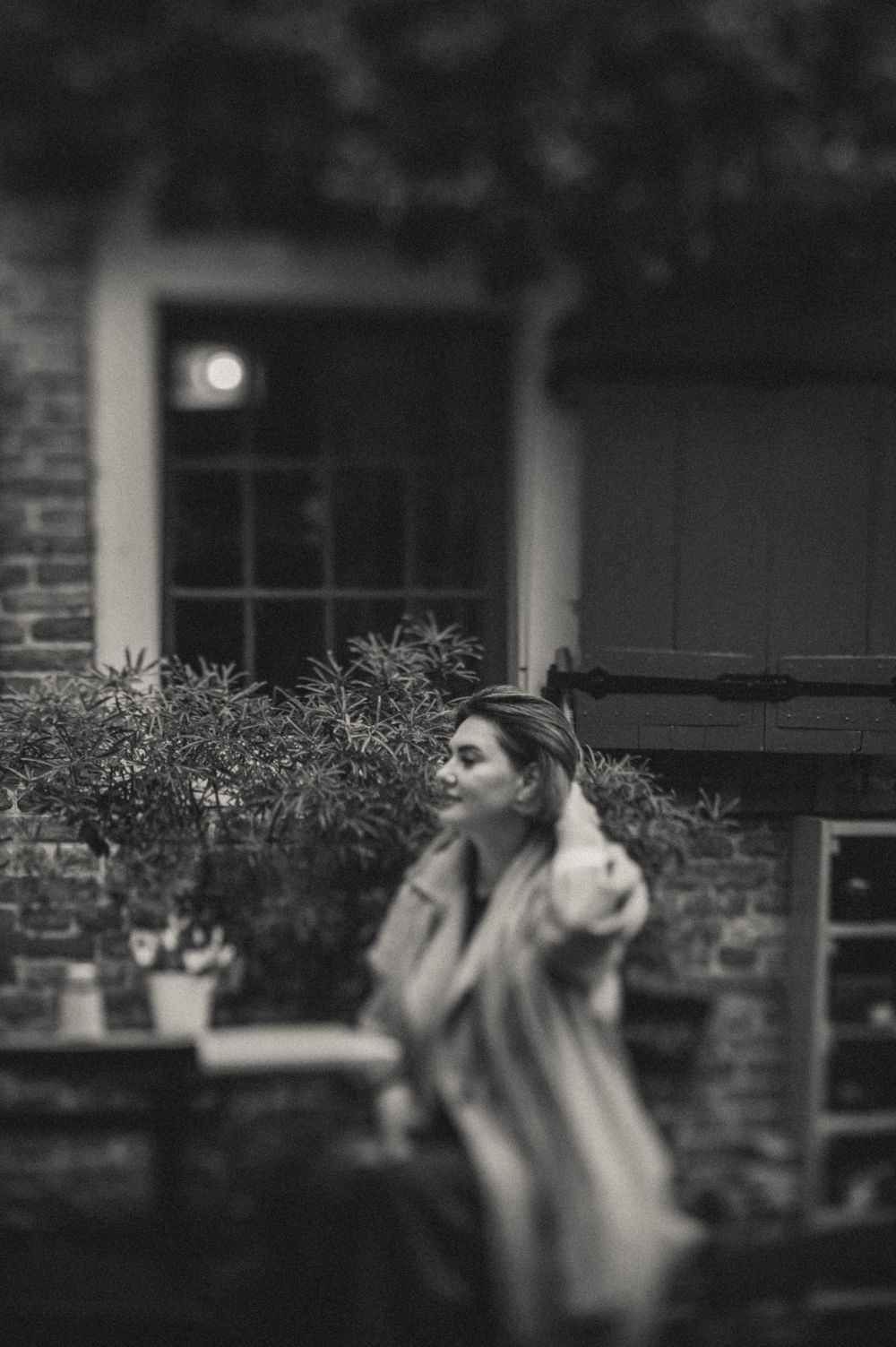 Artistic black and white portrait through foliage and garden elements.