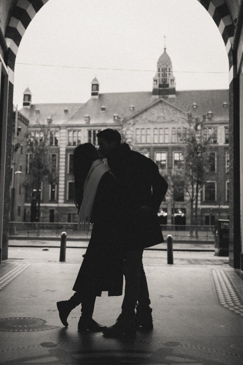 Silhouettes of people walking under an archway with historic buildings in the background.