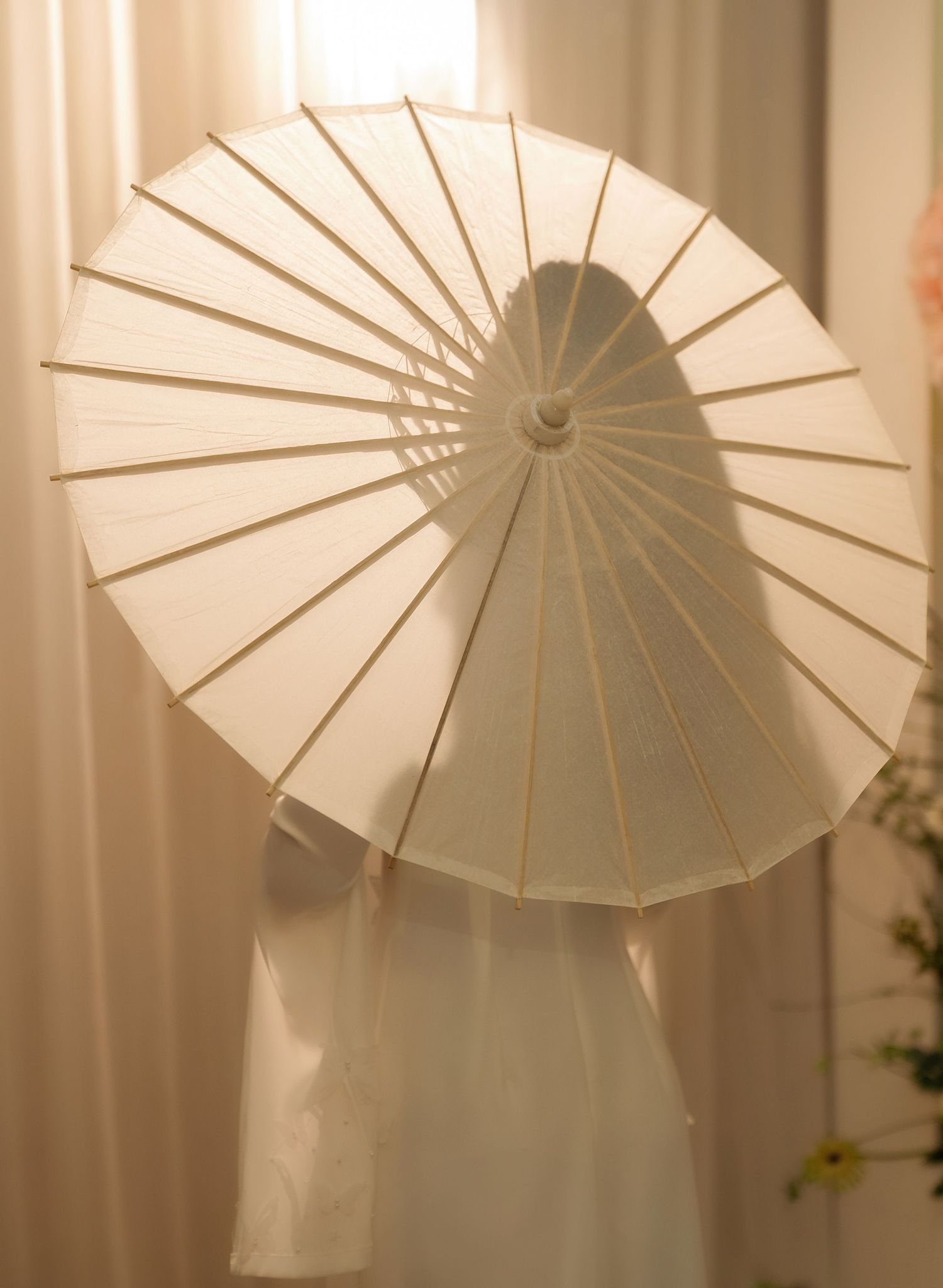 A white paper parasol casts delicate shadows against a light curtain background.