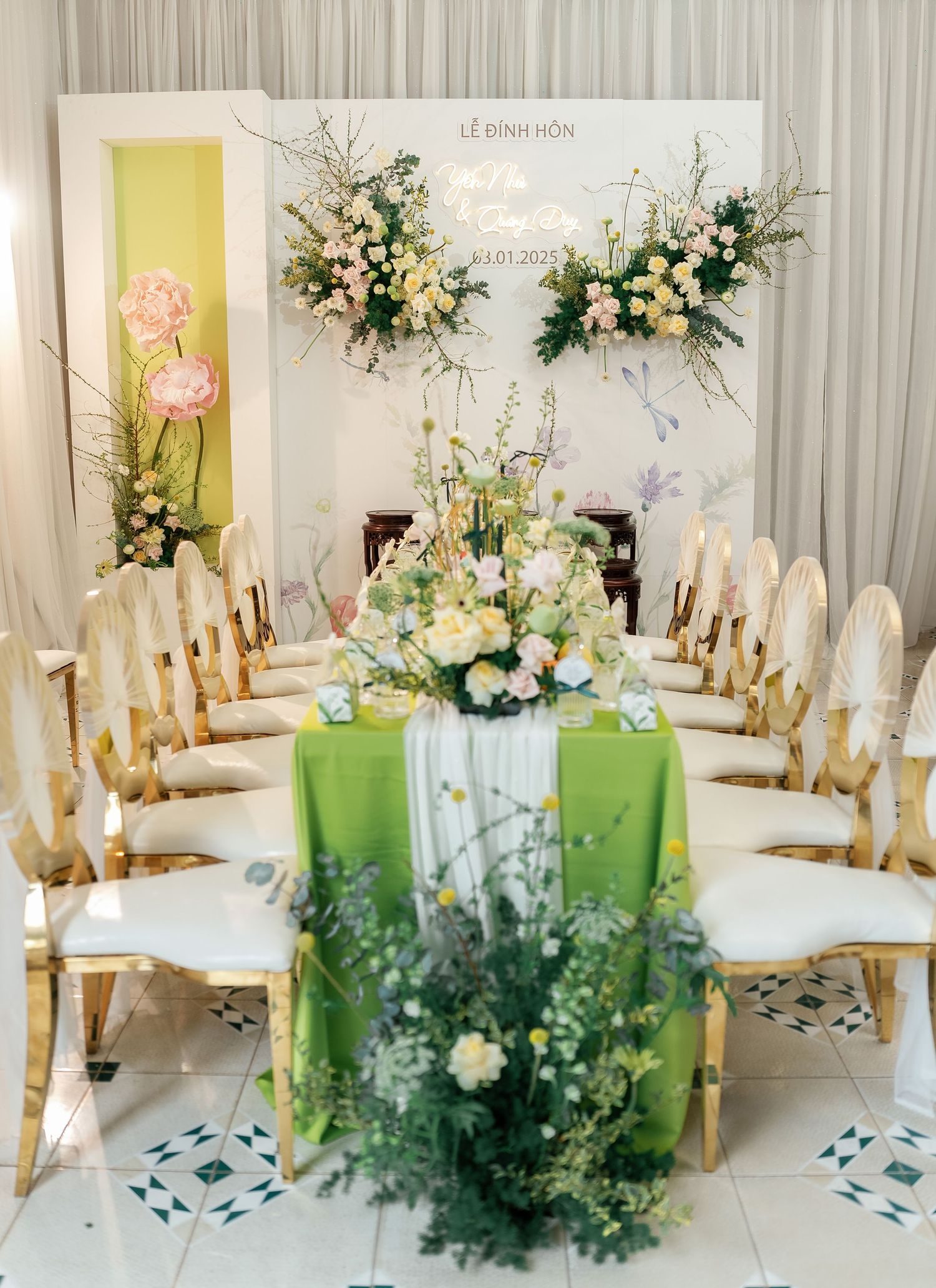 Elegant wedding table setting with cream chairs, lime green tablecloth, and white floral arrangements against draped backdrop.
