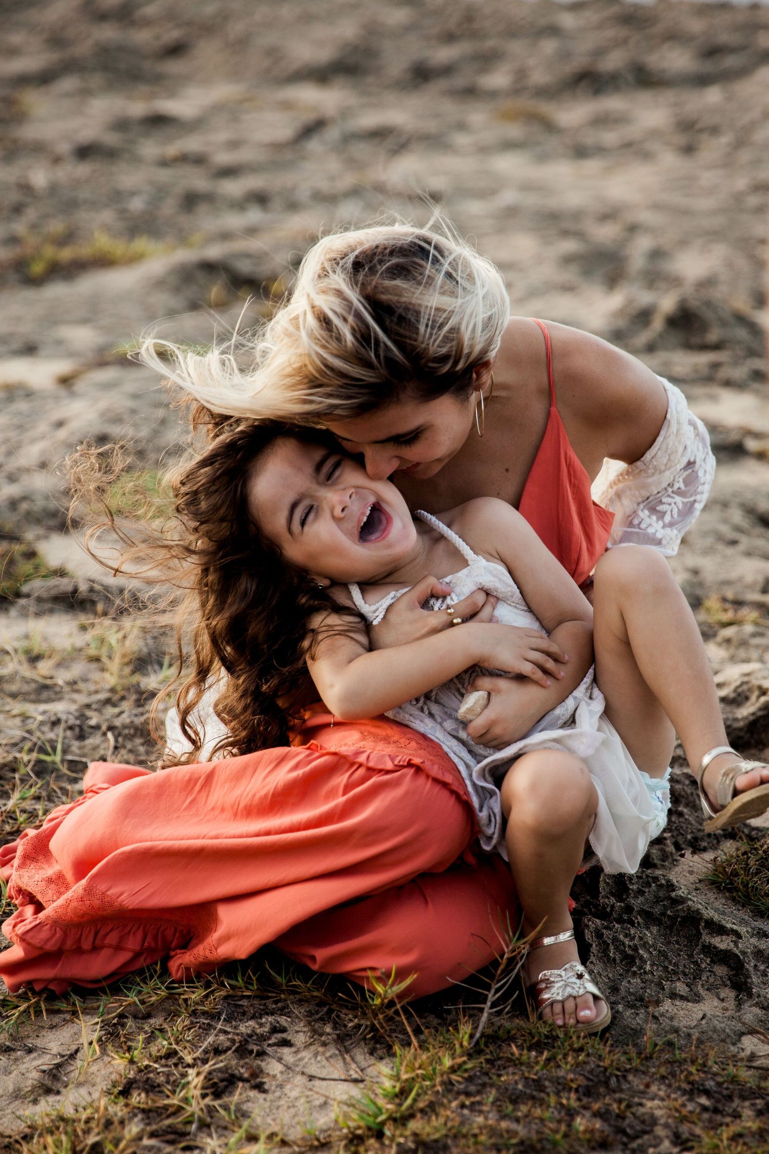 A joyful moment shared between a mother and daughter laughing and embracing on rocky terrain at sunset. SLC, Utah.