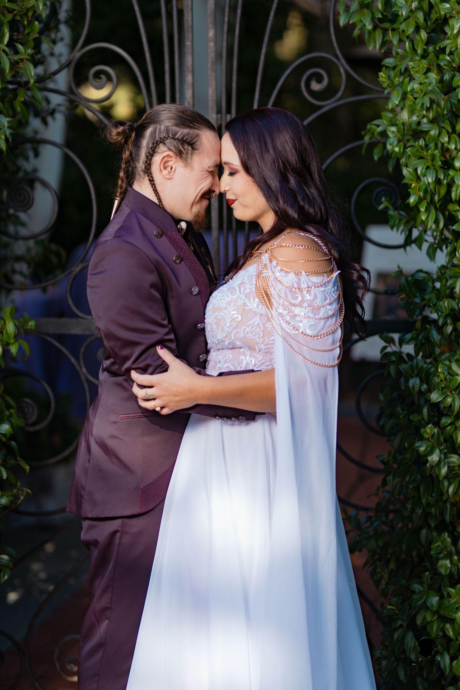 Romantic wedding portrait of a couple embracing in front of an ornate gate with greenery.