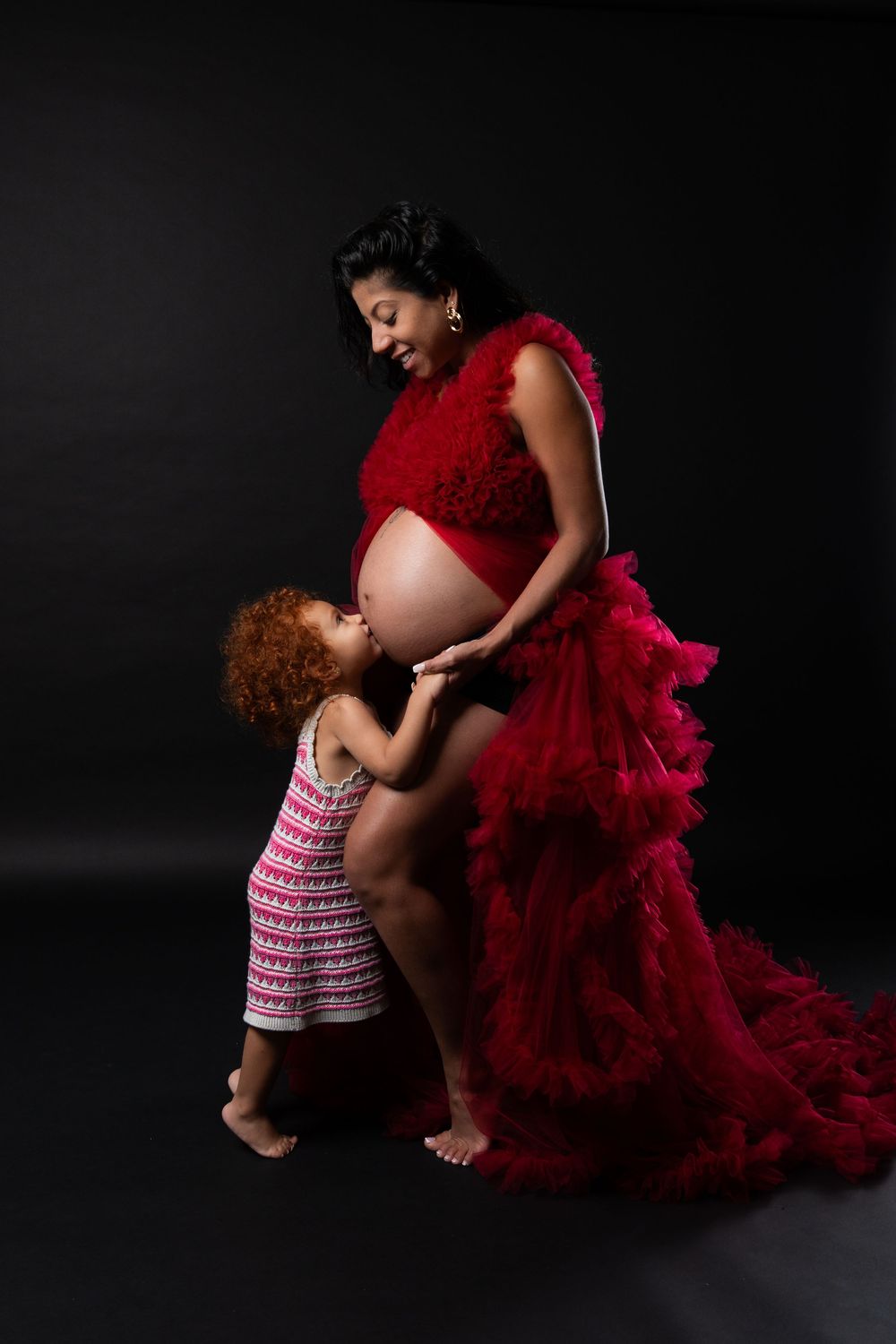 A series of maternity photos showing a tender moment between parent and child against a dark background with a flowing red dress.