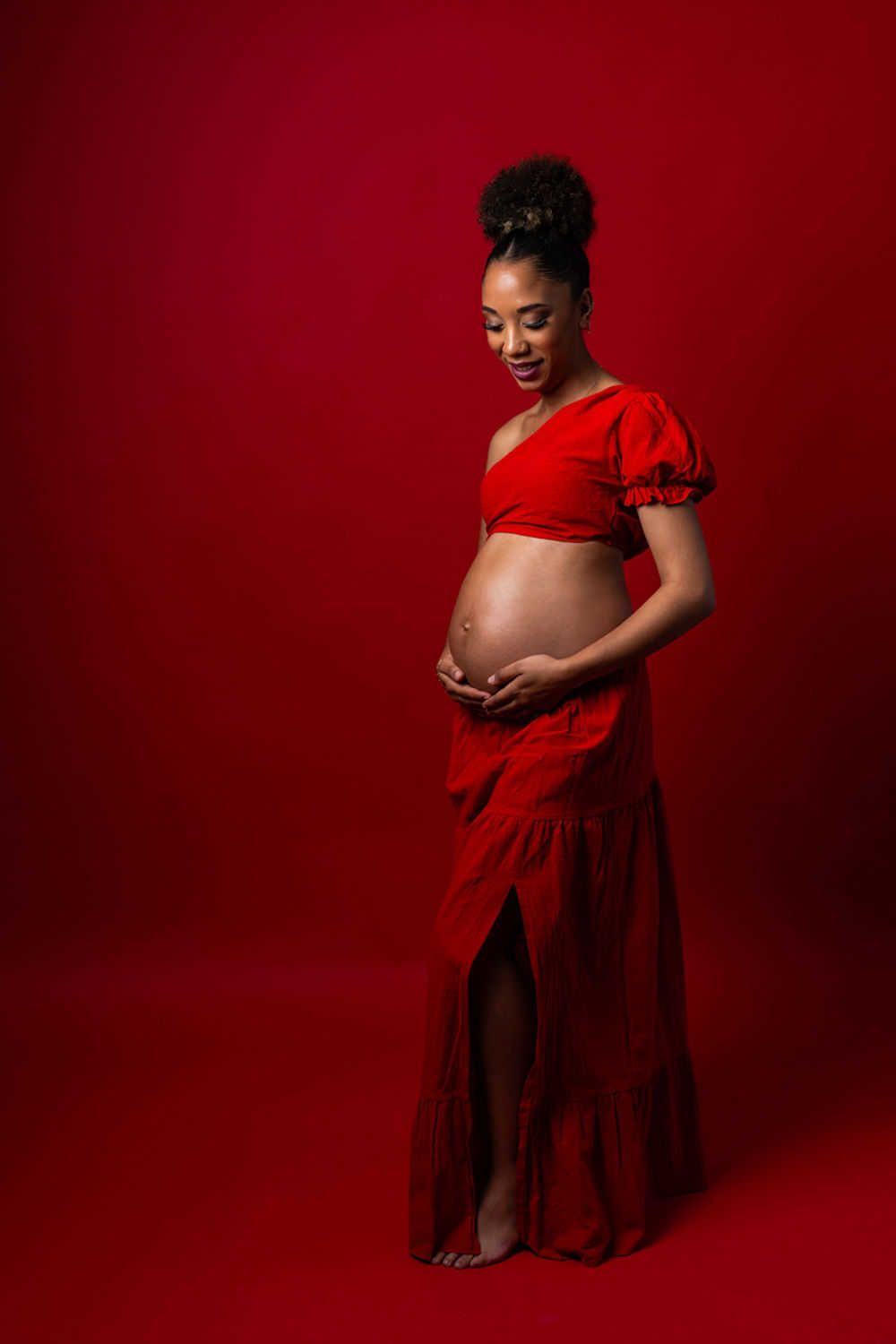 Une silhouette pleine d'espoir dans une robe rouge fluide pose joyeusement sur un fond rouge pour une séance photo de maternité.