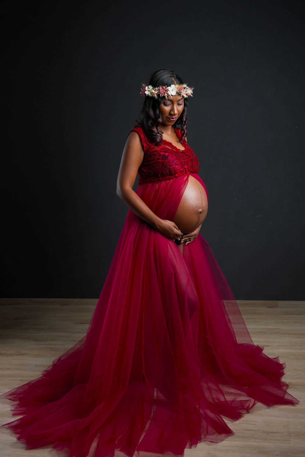 Belle robe de maternité en tulle bordeaux avec couronne florale et traîne fluide lors d'une séance photo spectaculaire en studio.