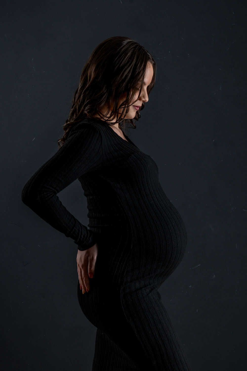 Silhouette d'une silhouette enceinte en robe noire sur fond sombre montrant une pose de profil latéral dramatique.