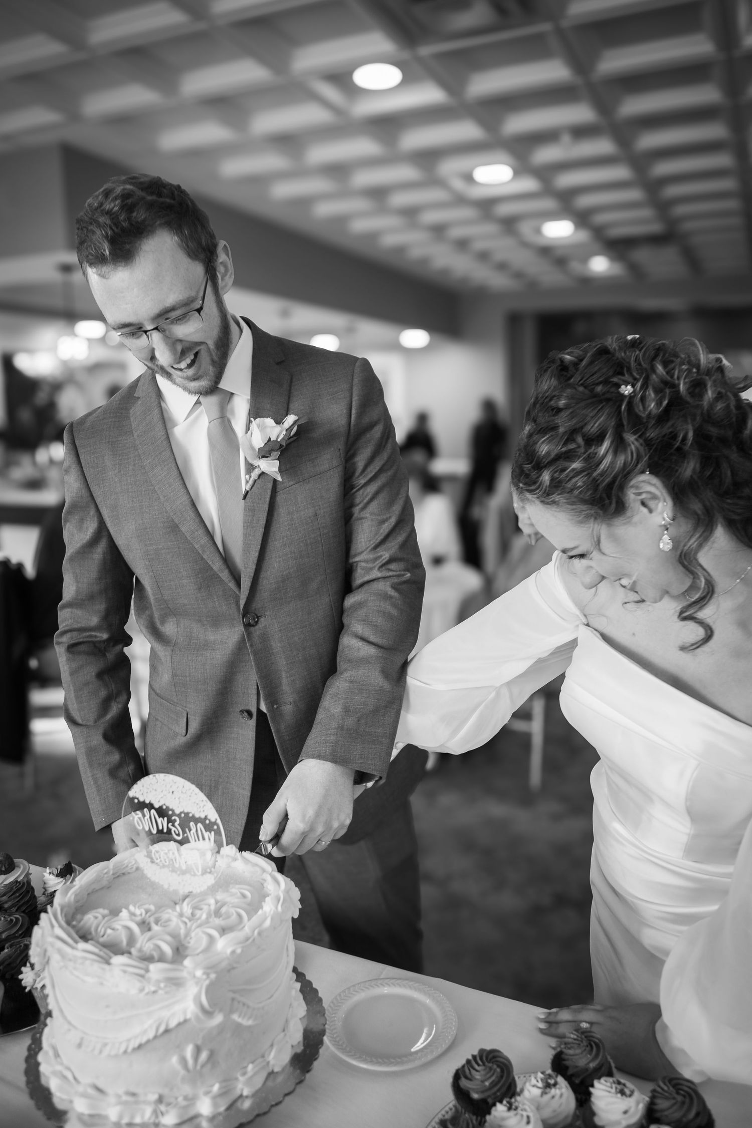 Happy couple shares a joyful moment while cutting their white wedding cake at their reception.