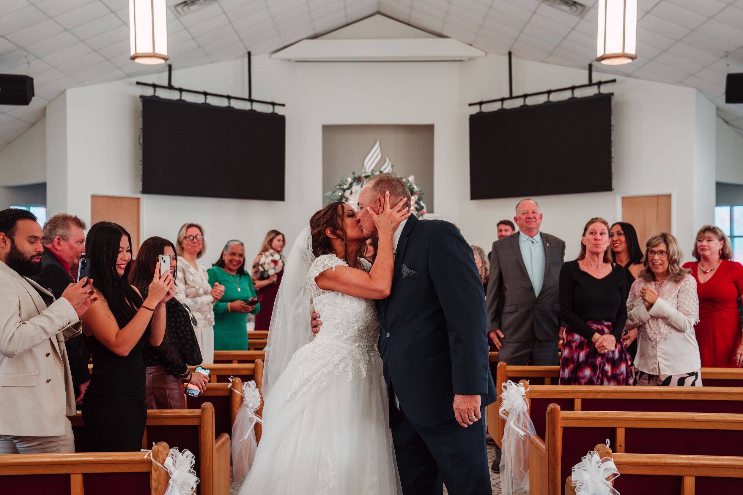 A joyous wedding ceremony kiss in a church with guests applauding.