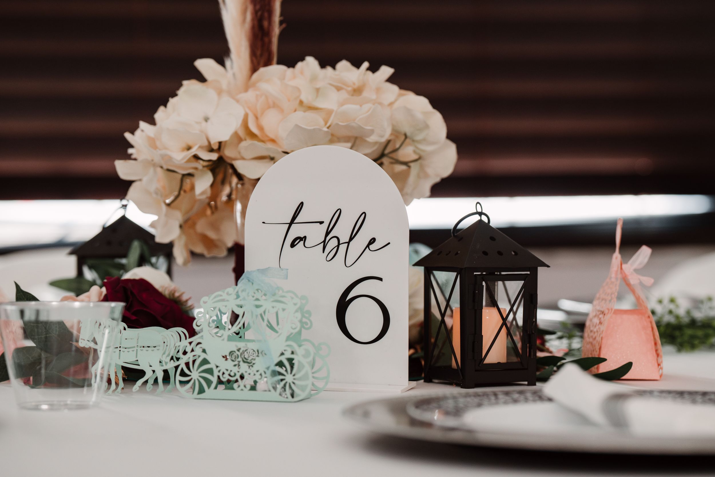 Elegant table setting with black lantern, floral centerpiece and table number 6.