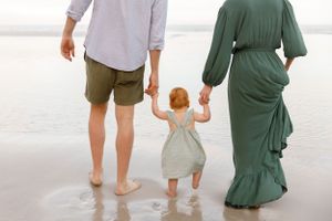 A family walks barefoot together on a sandy beach with waves in the background.