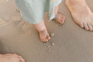 Small bare feet leave footprints in wet sand on a beach alongside adult feet.