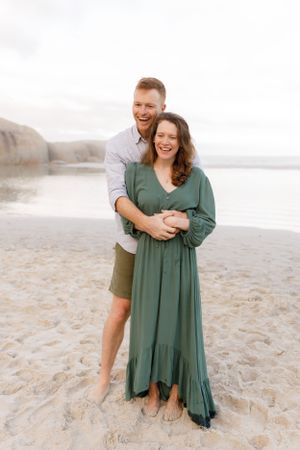 A joyful couple embraces on the beach, with the woman wearing a flowing green dress.