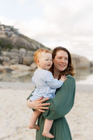 A tender moment between a parent and child on a scenic beach with rocky cliffs in the background.